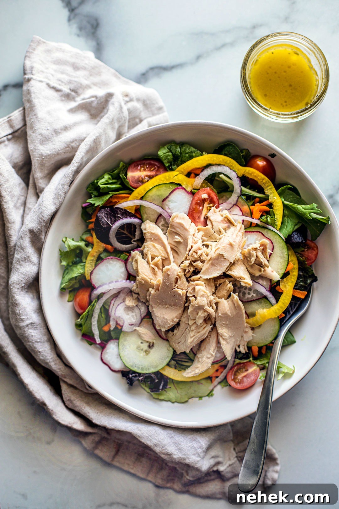 Overhead shot of seasonal vegetable salad topped with big chunks of tuna; homemade dressing on the side.