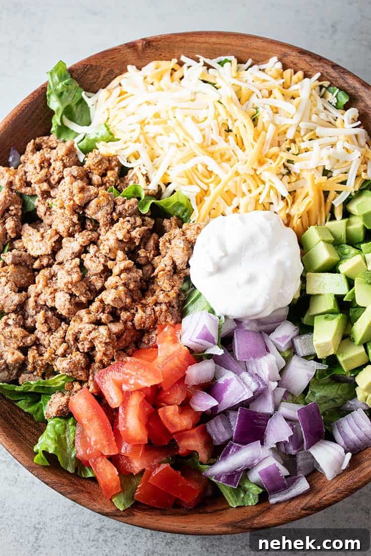 overhead view of turkey taco salad in a wooden bowl with sections of ground turkey, cheese, chopped avocado, chopped tomato, chopped onions and sour cream in the middle, all on a bed of lettuce