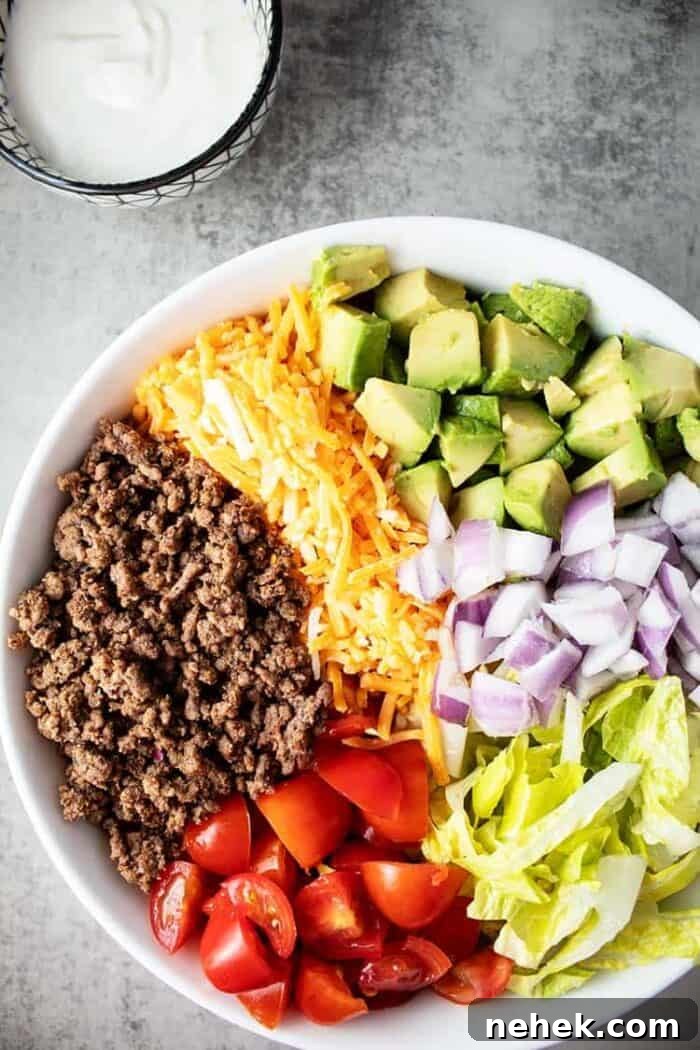 large white bowl containing keto taco salad next to a small bowl containing sour cream