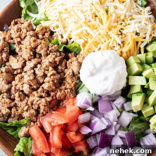 overhead view of turkey taco salad in a wooden bowl with sections of ground turkey, cheese, chopped avocado, chopped tomato, chopped onions and sour cream in the middle, all on a bed of lettuce