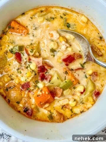 Corn soup with sweet potatoes and bacon in a bowl with a spoon.
