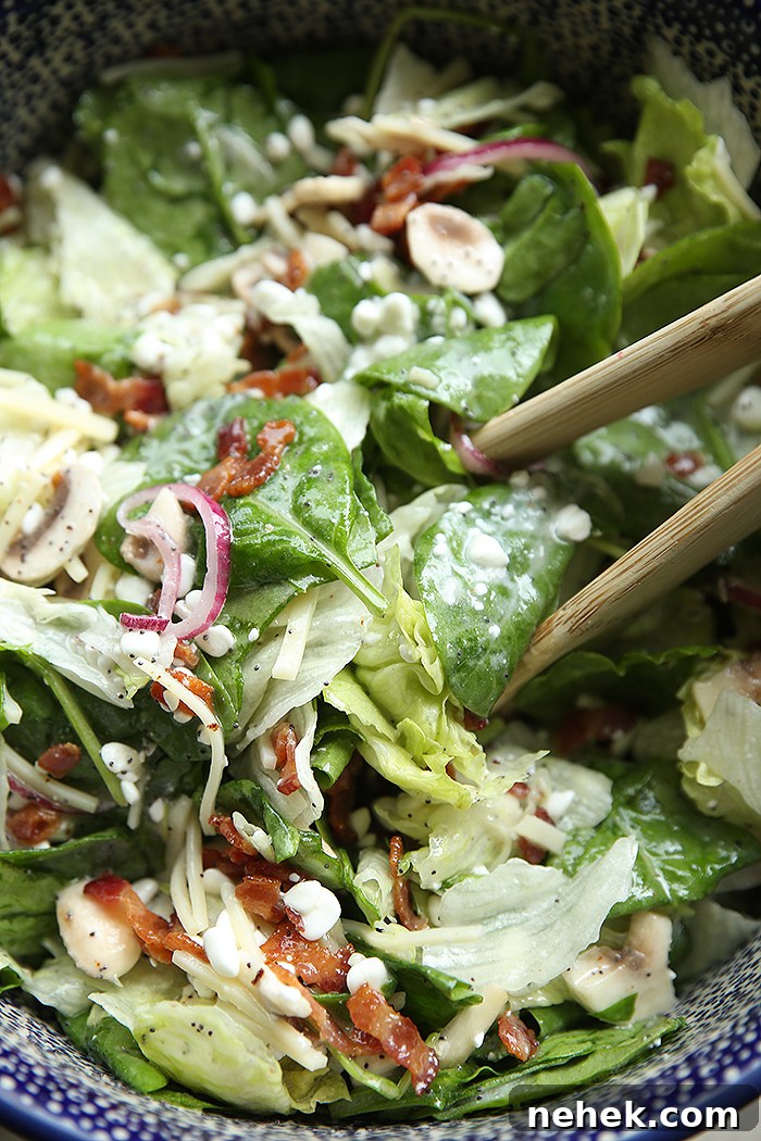A large Polish potter bowl of Spinach Poppy Seed Salad with wooden salad tongs inserted from the right.