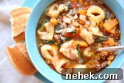 Blue bowl with sausage tortellini soup with sweet potatoes. A spoon is in the bowl and bread on the side.