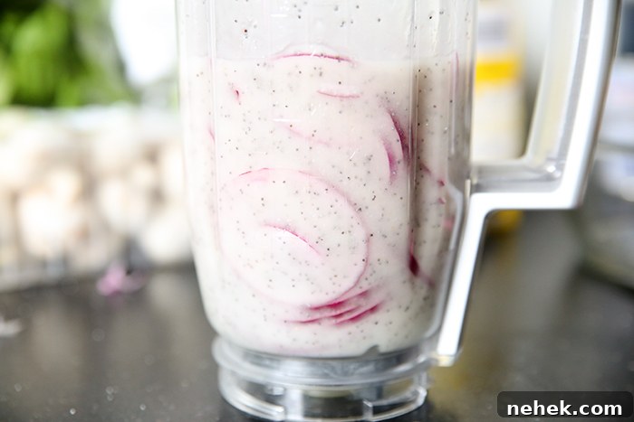 A blender full of poppy seed dressing with picked red onions.