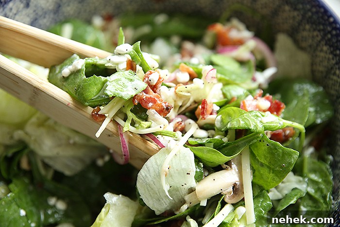 Spinach poppy seed salad in a large bowl with wooden tongs angled from the left grabbing a serving of salad.
