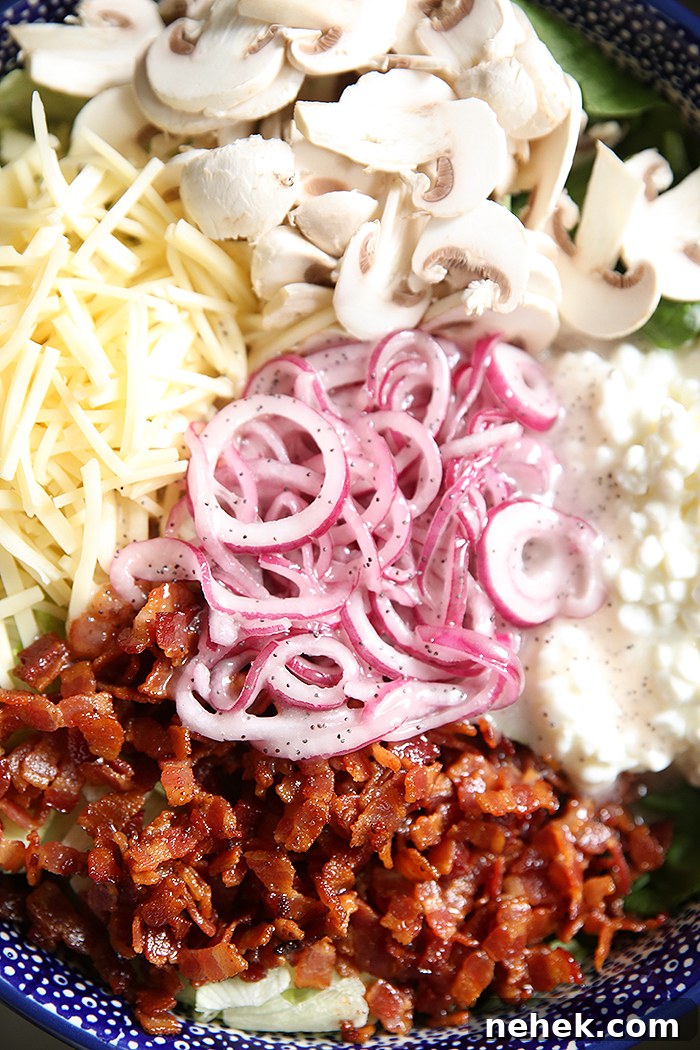 A large serving bowl with spinach, chopped iceberg lettuce, bacon crumbles, marinated red onions, cottage cheese, Swiss cheese and sliced mushrooms.