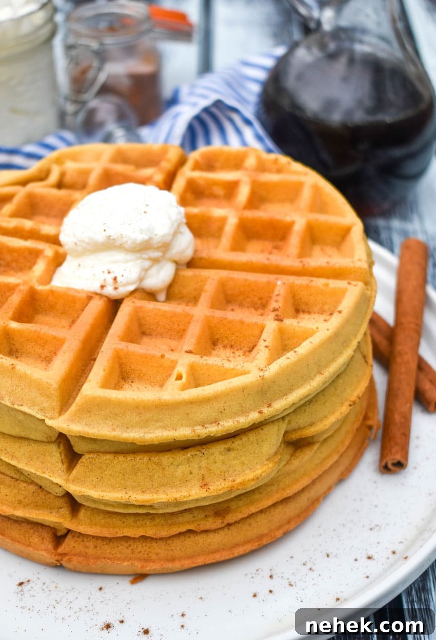 a stack of pumpkin spice waffles topped with whipped cream on a white plate