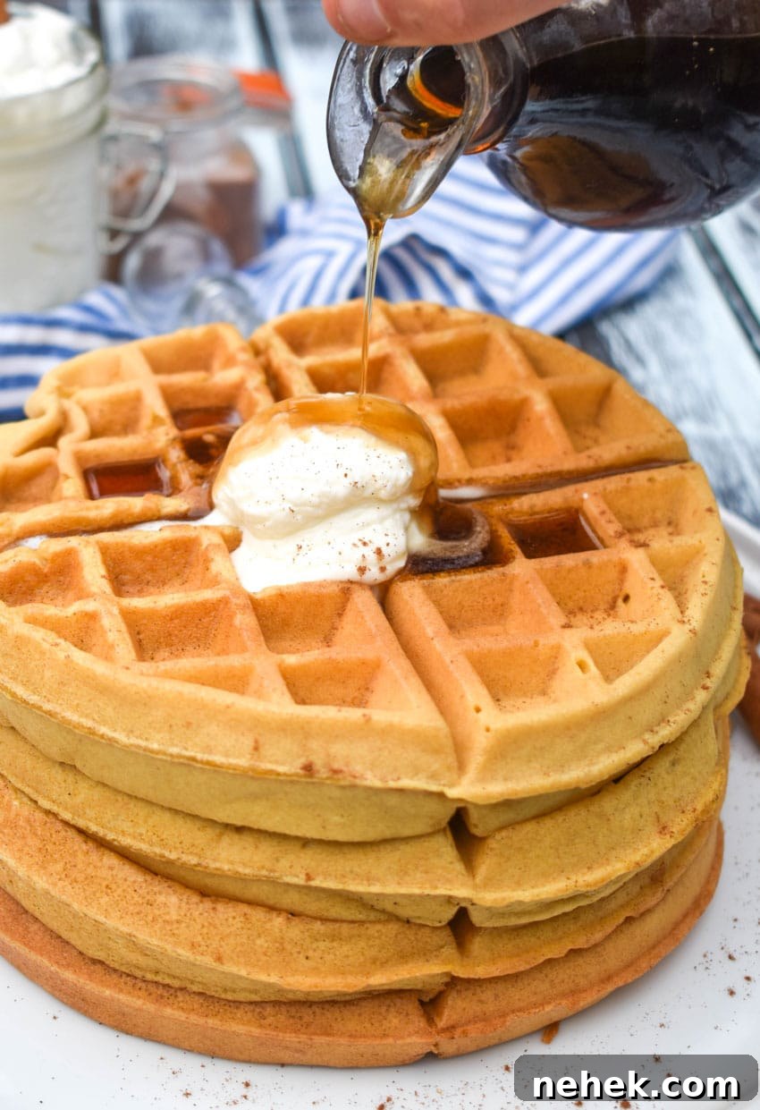 syrup being poured over a stack of pumpkin spice waffles on a white plate