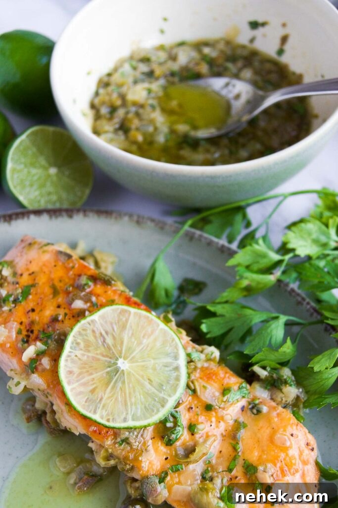 a plate holds a filet of salmon topped with capere sauce for fish and a wheel of lime