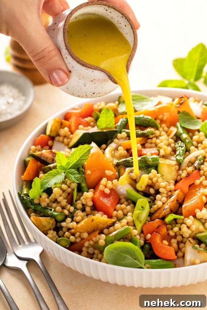 Israeli couscous and grilled vegetables salad getting drizzled with vinaigrette