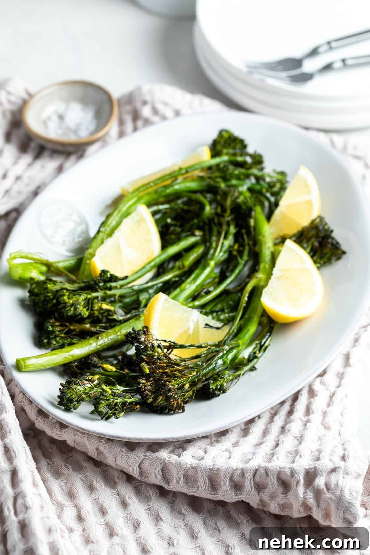 White dish with cooked broccolini garnished with lemon wedges.