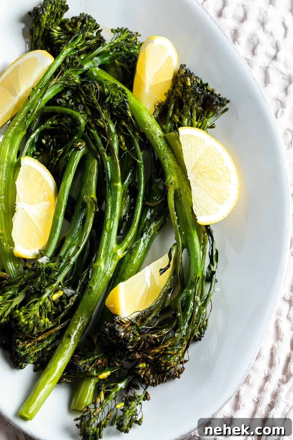 White dish with cooked broccolini garnished with lemon wedges.