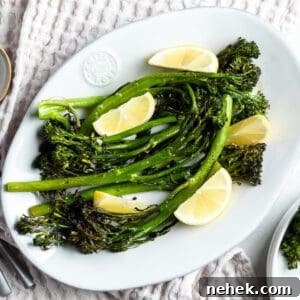 White dish with cooked broccolini garnished with lemon wedges.