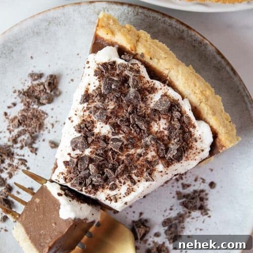 overhead view of keto chocolate pie topped with sugar free whipped cream and chocolate shavings on a swerving dish with a gold fork