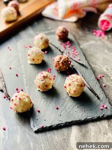 milk and chocholate cake pops on a black slate with two vanilla pods and scattered little pink sugar hearts