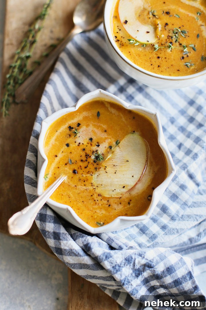 close up of a white bowl and spoon with butternut squash soup and apple