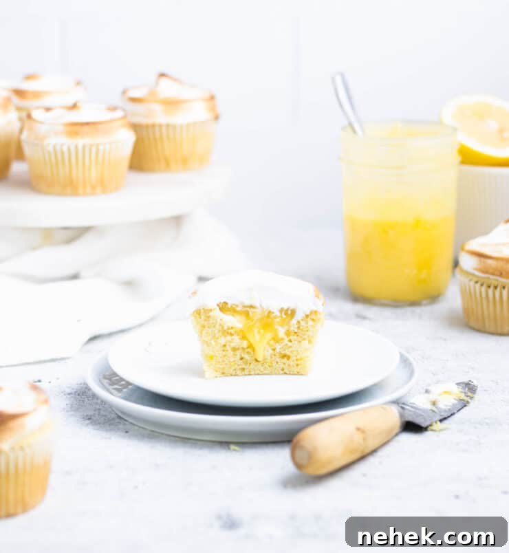 How to Fill Cupcakes Perfectly: 6 Methods for Delicious Centers 2 Halved lemon meringue cupcake with filling dripping out onto a white plate. Lemon curd, bowl of lemons and cupcakes in the background.