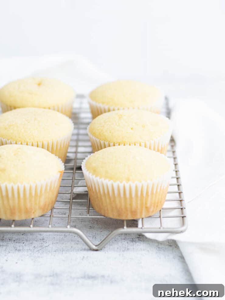 How to Fill Cupcakes Perfectly: 6 Methods for Delicious Centers 3 Lemon cupcakes in white liners on a gold cooling rack.