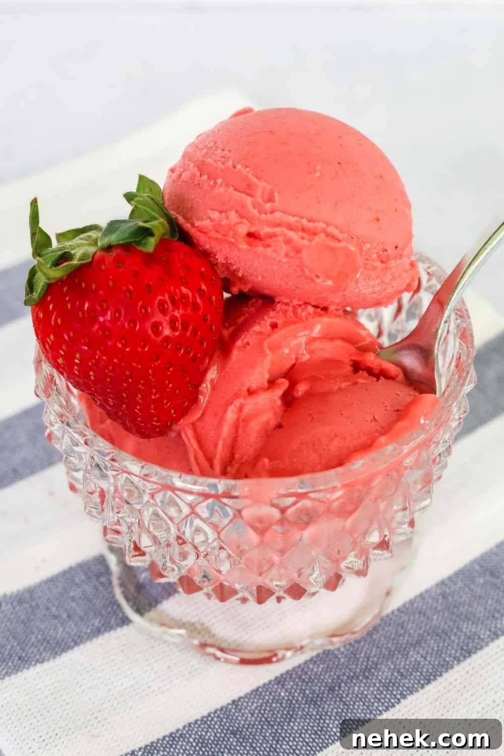 close-up view of scoops of fresh strawberry sorbet served in a glass dessert cup, garnished with a fresh strawberry.