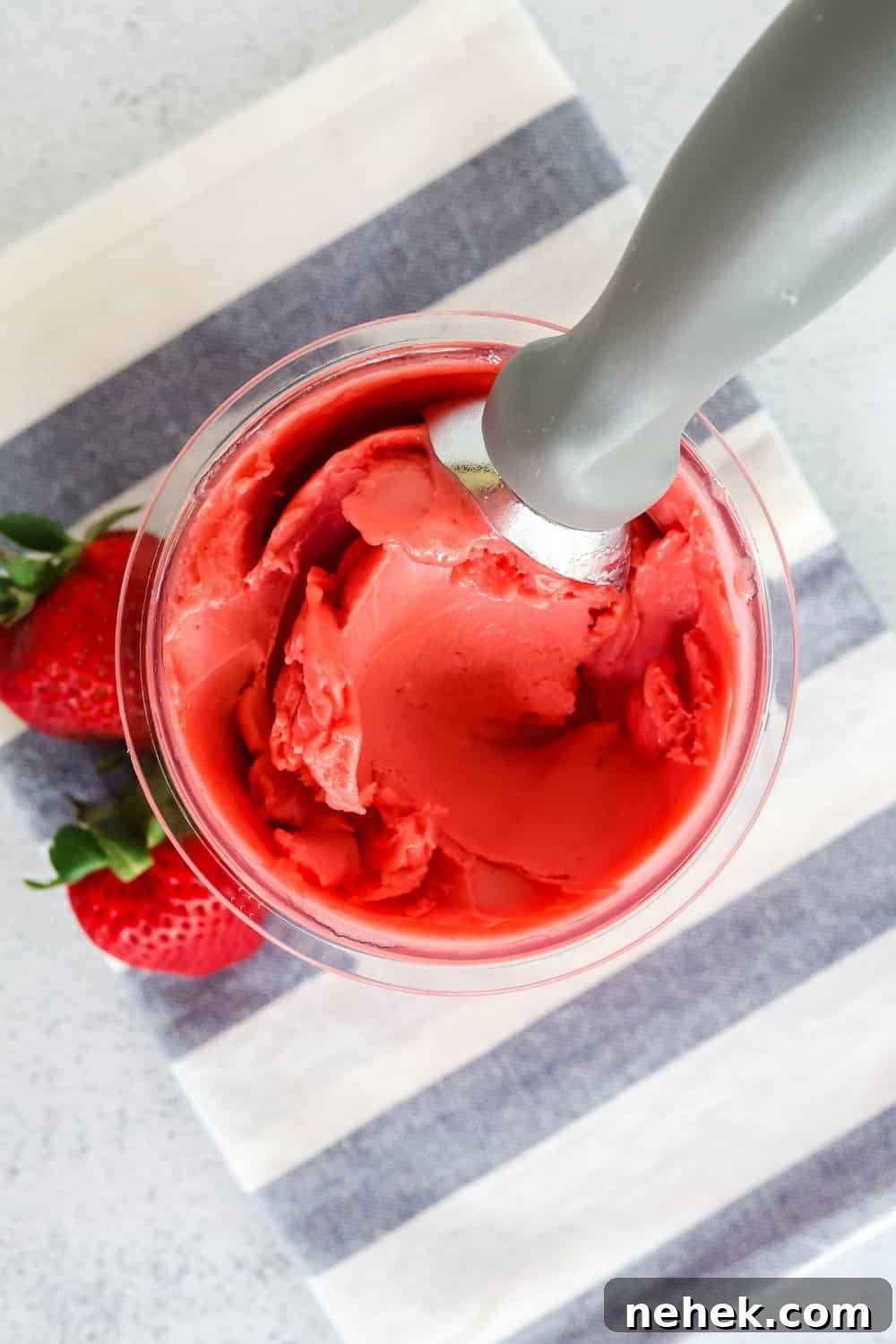 overhead view of a pint of strawberry sorbet made in the Ninja Creami. Two fresh strawberries are next to the pint container.
