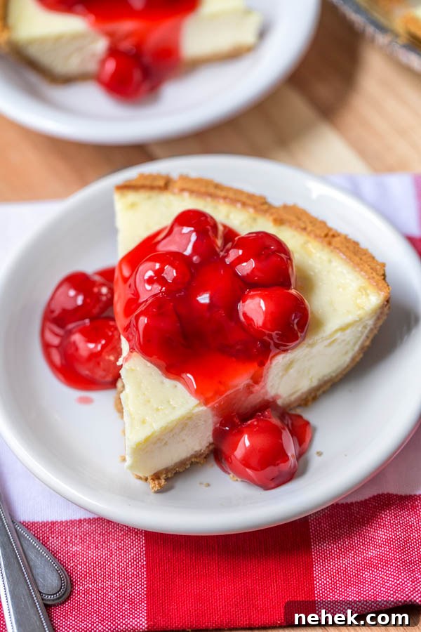 easy cheesecake recipe of a slice of cheesecake on a white plate with cherry pie filling
