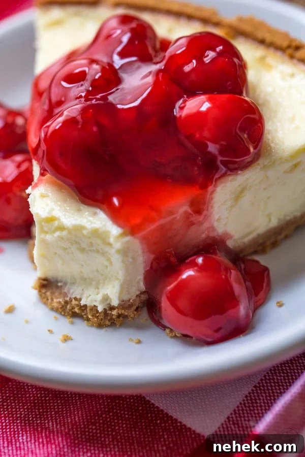 easy cheesecake recipe of a slice of cheesecake on a white plate with cherry pie filling