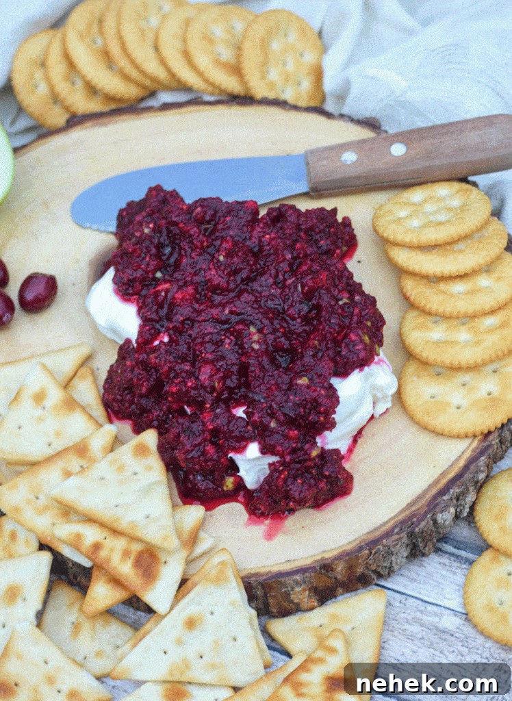 Tangy Cranberry Salsa Recipe for Holidays and Entertaining 4 cranberry salsa spread over a softened block of cream cheese on a wooden cutting board surrounded by crackers