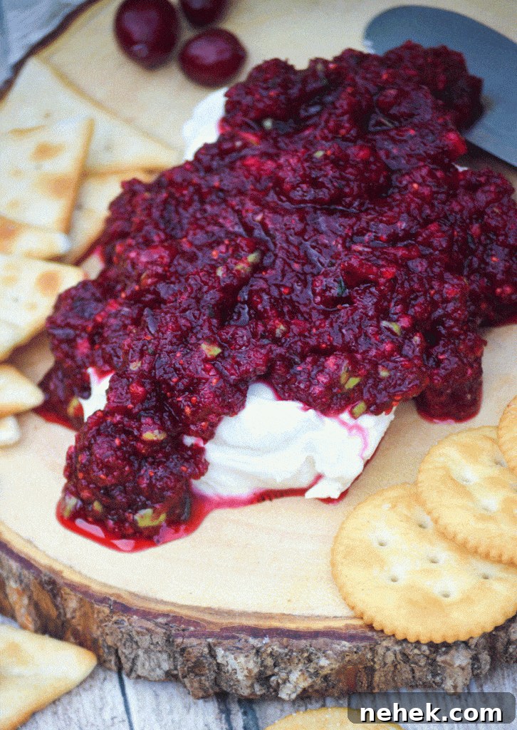 Tangy Cranberry Salsa Recipe for Holidays and Entertaining 5 cranberry salsa spread over a softened block of cream cheese on a wooden cutting board surrounded by crackers