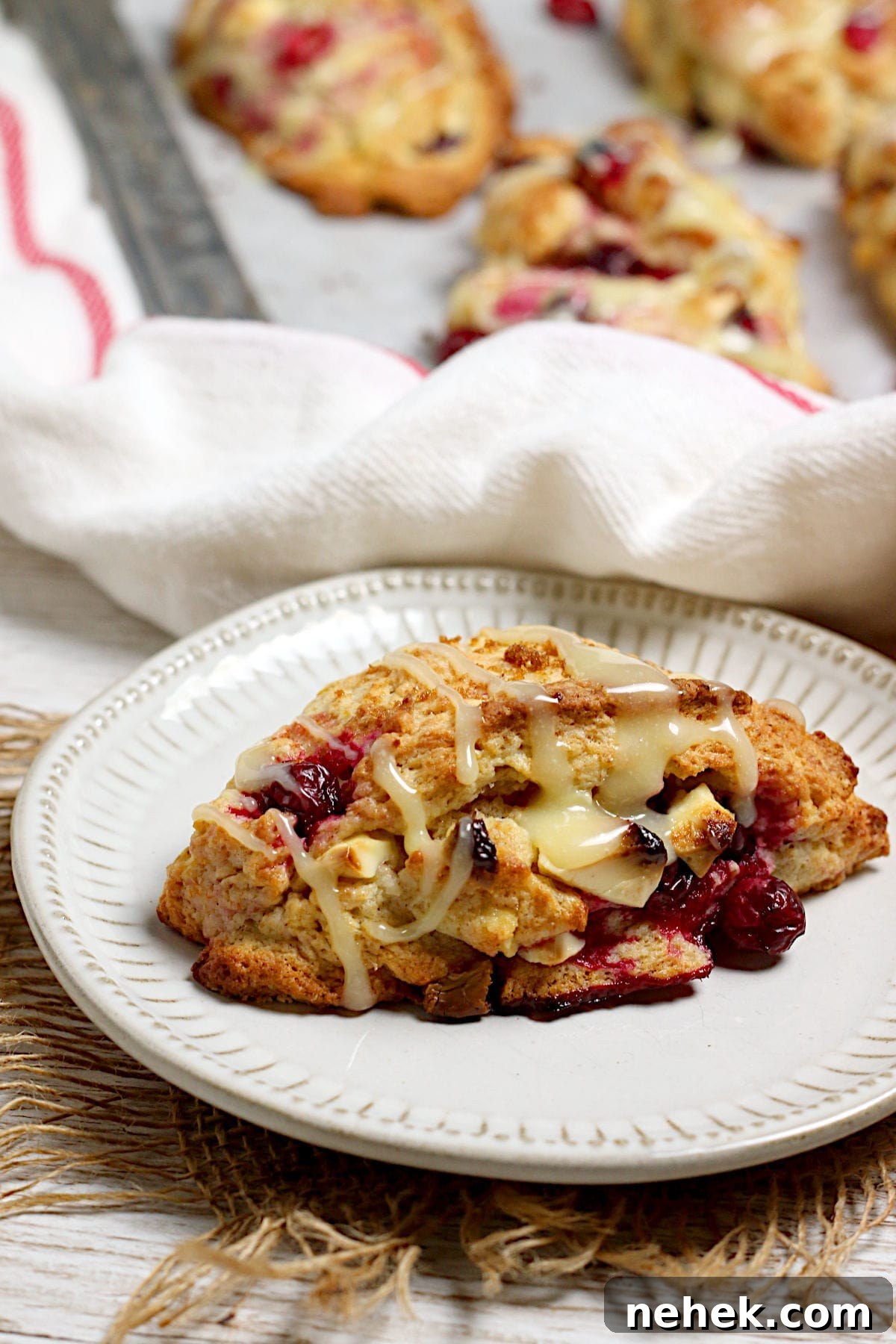 Cranberry Orange Scones with White Chocolate Drizzle 5 A closeup photo of a Cranberry Orange Scone with White Chocolate on a small white plate.