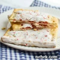 A pop tart, broken in half, resting on top of a full sized pop tart on a plate.