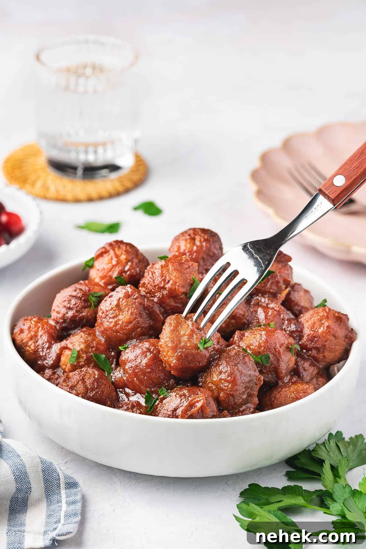 A fork piercing into a cranberry meatball in a bowl.