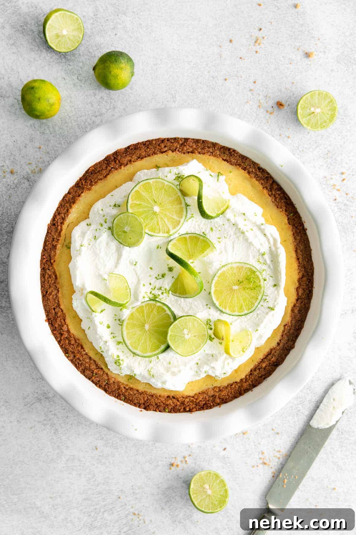Key lime pie on a countertop, surrounded by fresh limes and a knife.