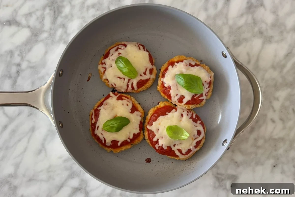 Chicken Parmesan Burger Recipe: Crispy, Cheesy Sandwiches 8 Chicken parmesan burger patties topped with basil in a pan.