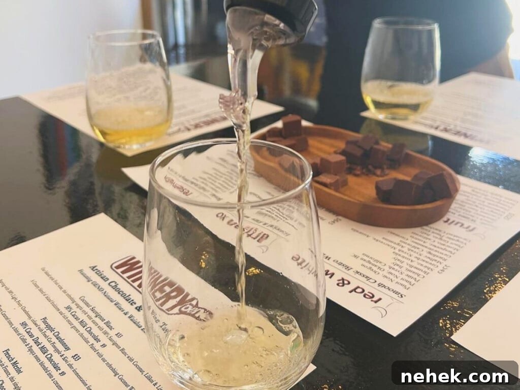 White wine being poured into a glass with chocolate and glasses of white wine on top of a table with menus in the background at Oeno winery in Kailua Hawaii.