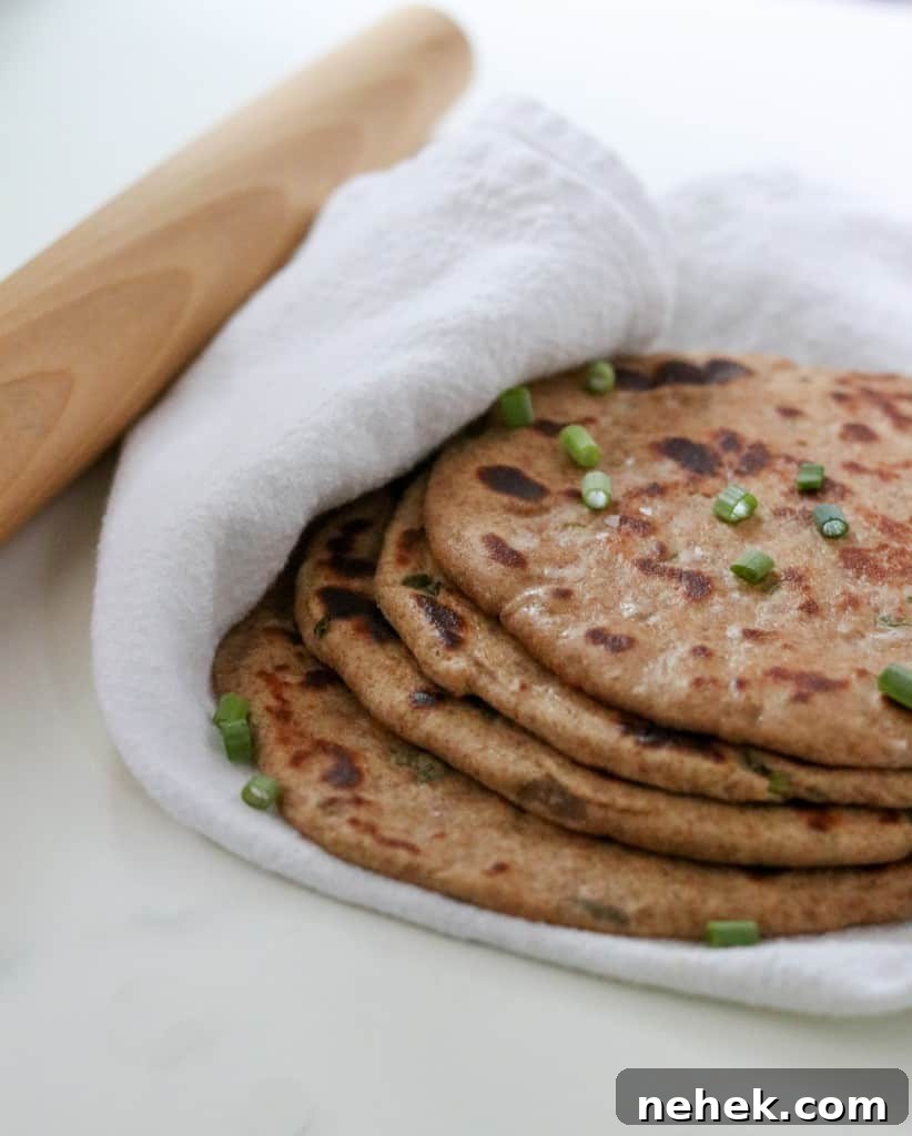 Flatbreads stacked on a towel next to a rolling pin