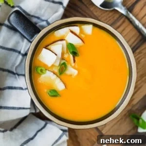 Overhead view of bright orange carrot soup with coconut and green onion garnish.