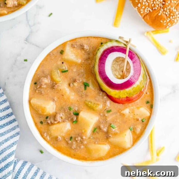 White round bowl of cheeseburger soup topped with onion, pickle, tomato.