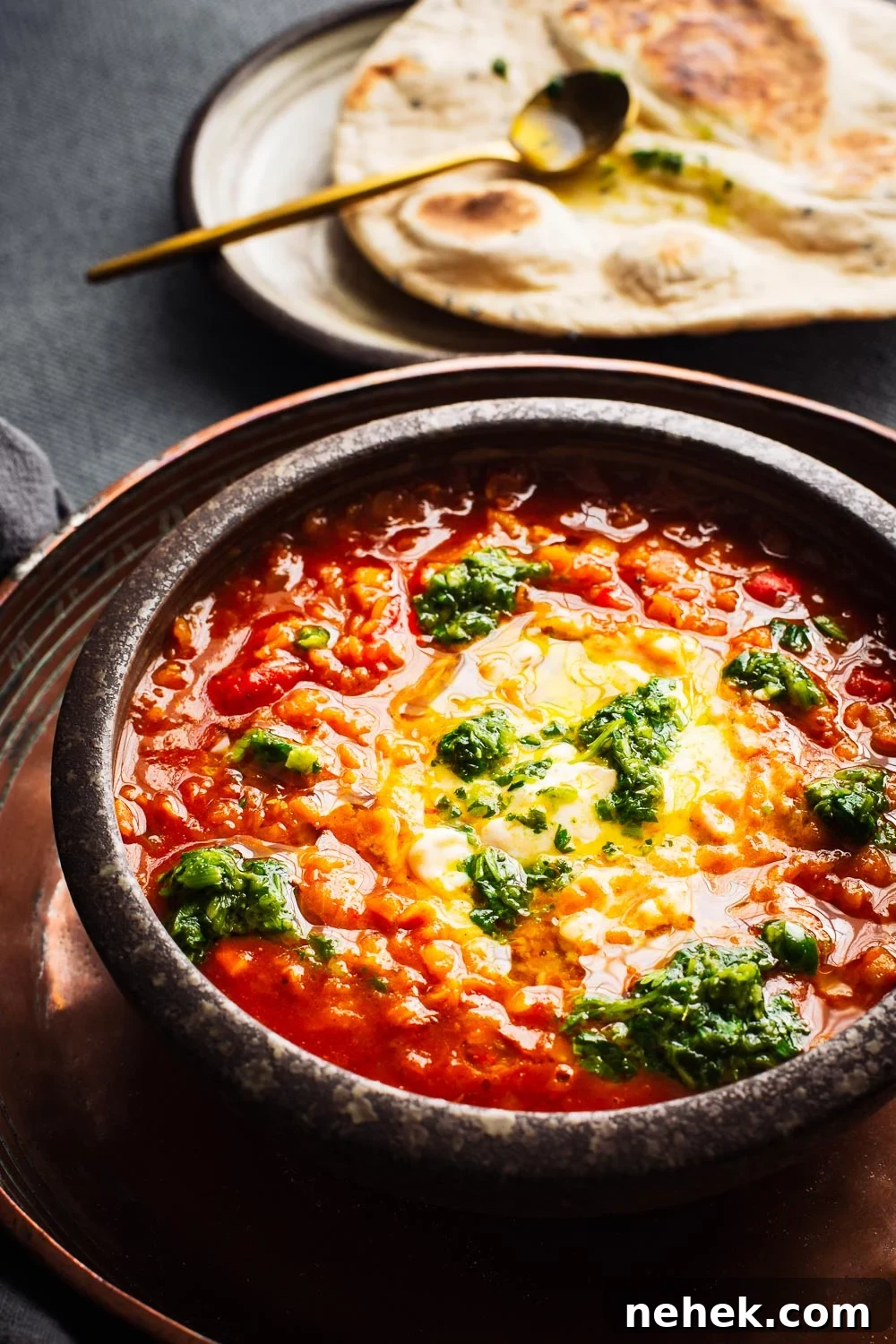 Close-up of a bowl of red lentil soup with a flatbread in the background.