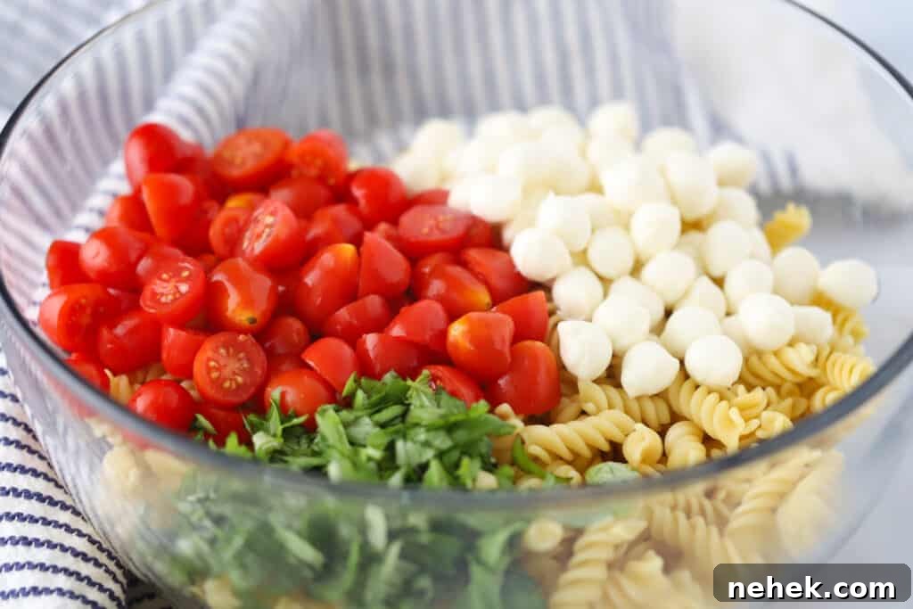 Caprese Pasta Salad Recipe: Fresh Tomato, Basil & Mozzarella 3 A glass mixing bowl filled with ingredients to make this mozzarella ball pasta salad, including cooked pasta, mozzarella balls, cherry tomatoes and fresh basil.