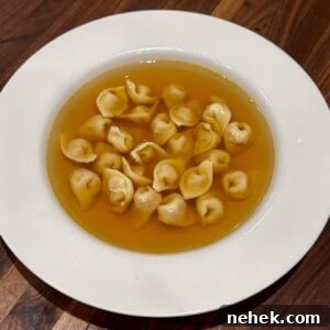Authentic Tortellini in Brodo: Classic Italian Soup Recipe 4 A white plate with a serving of tortellini in clear broth