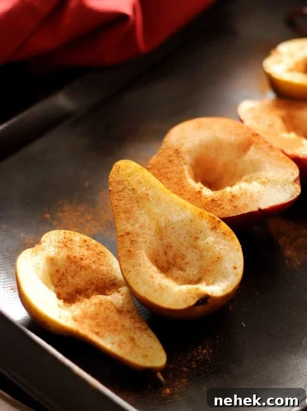 Maple Vanilla Baked Pears with Crunchy Granola Topping 6 Brown flexipan containing 5 pear halves with cinnamon sprinkled on top, red napkin in background.