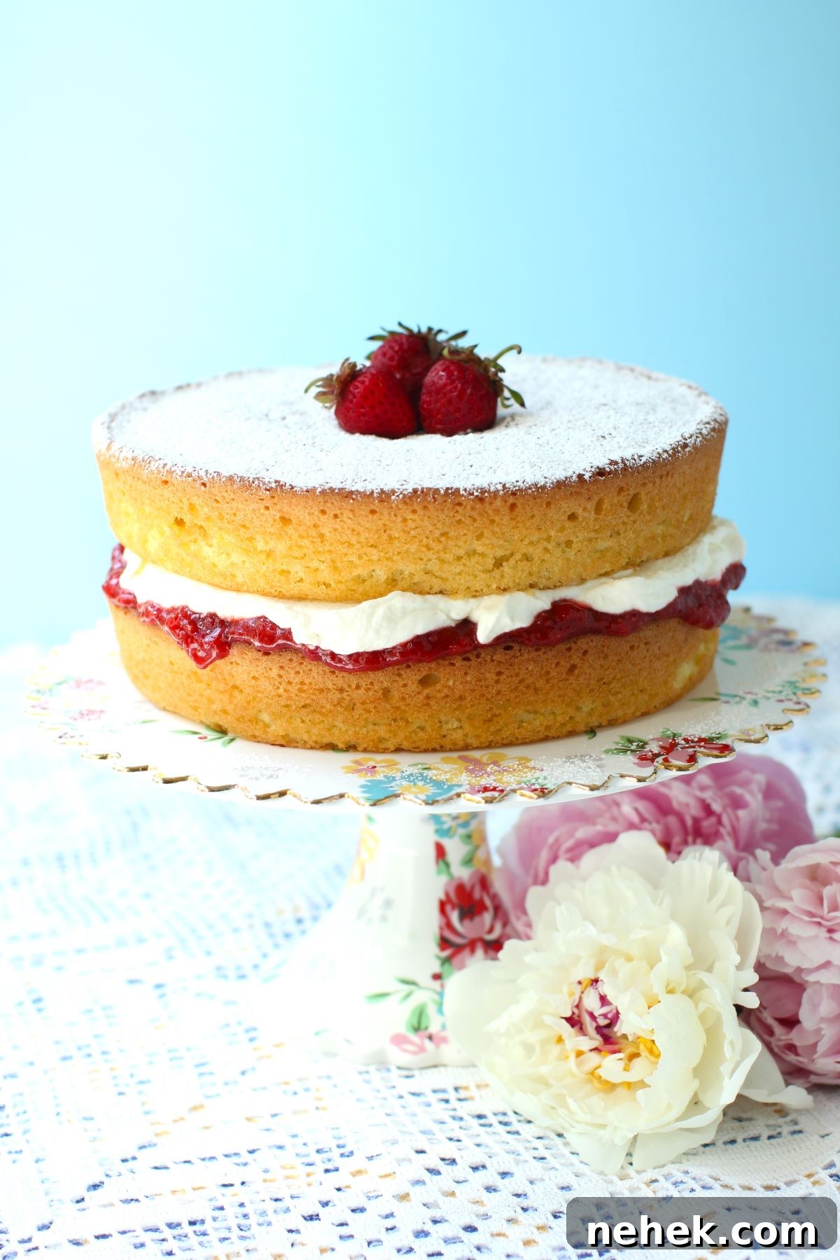 Gluten free Victoria Sponge cake on a cake stand with peonies laying beside it.