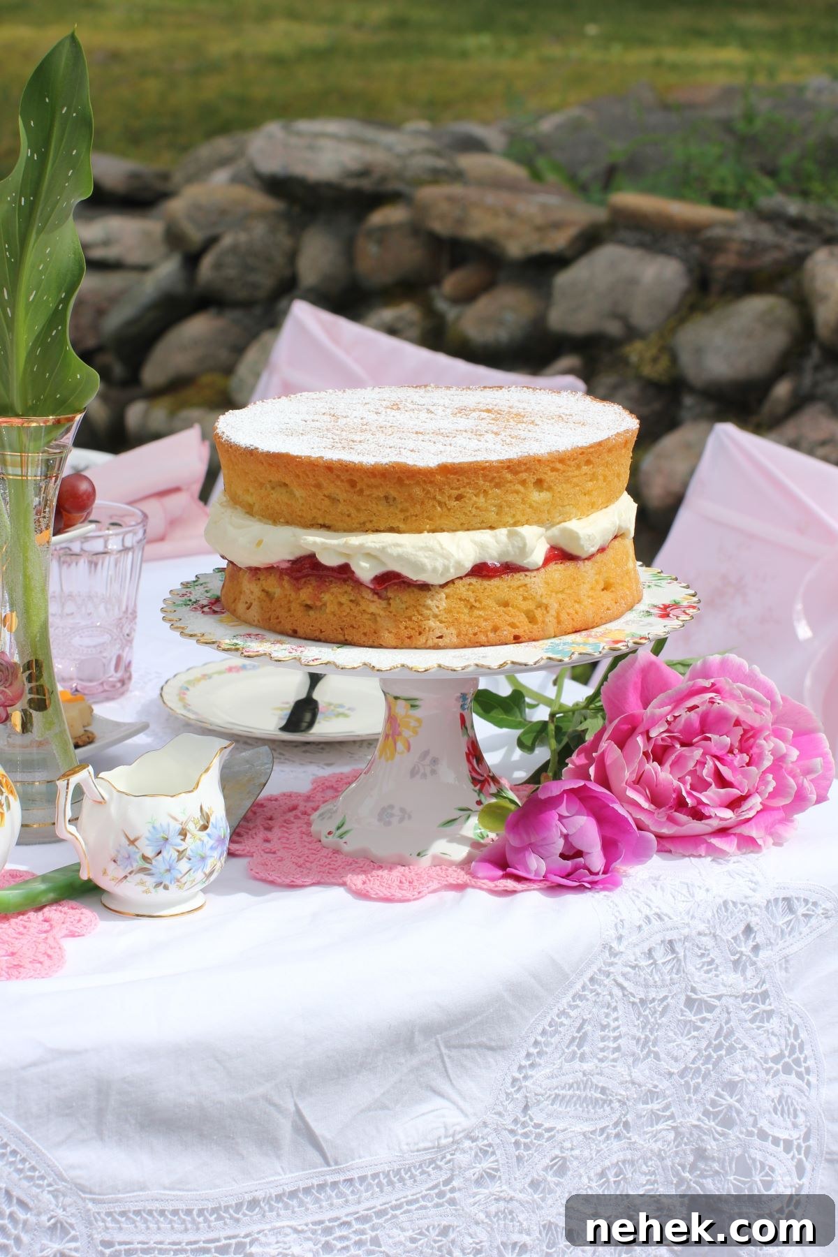 Gluten free Victoria Sponge cake on a cake stand on the lace-covered picnic table.
