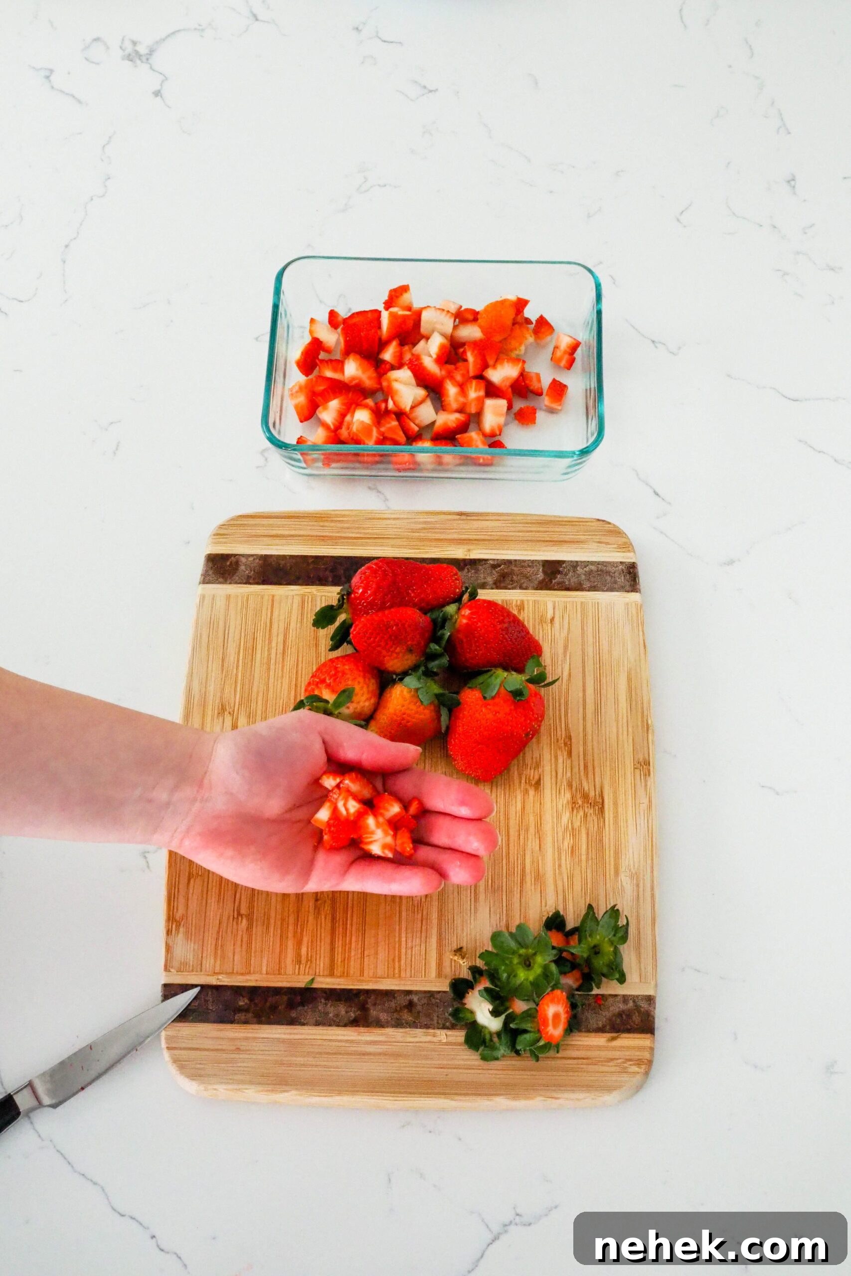 A hand holds up diced strawberries for strawberry champagne jam.