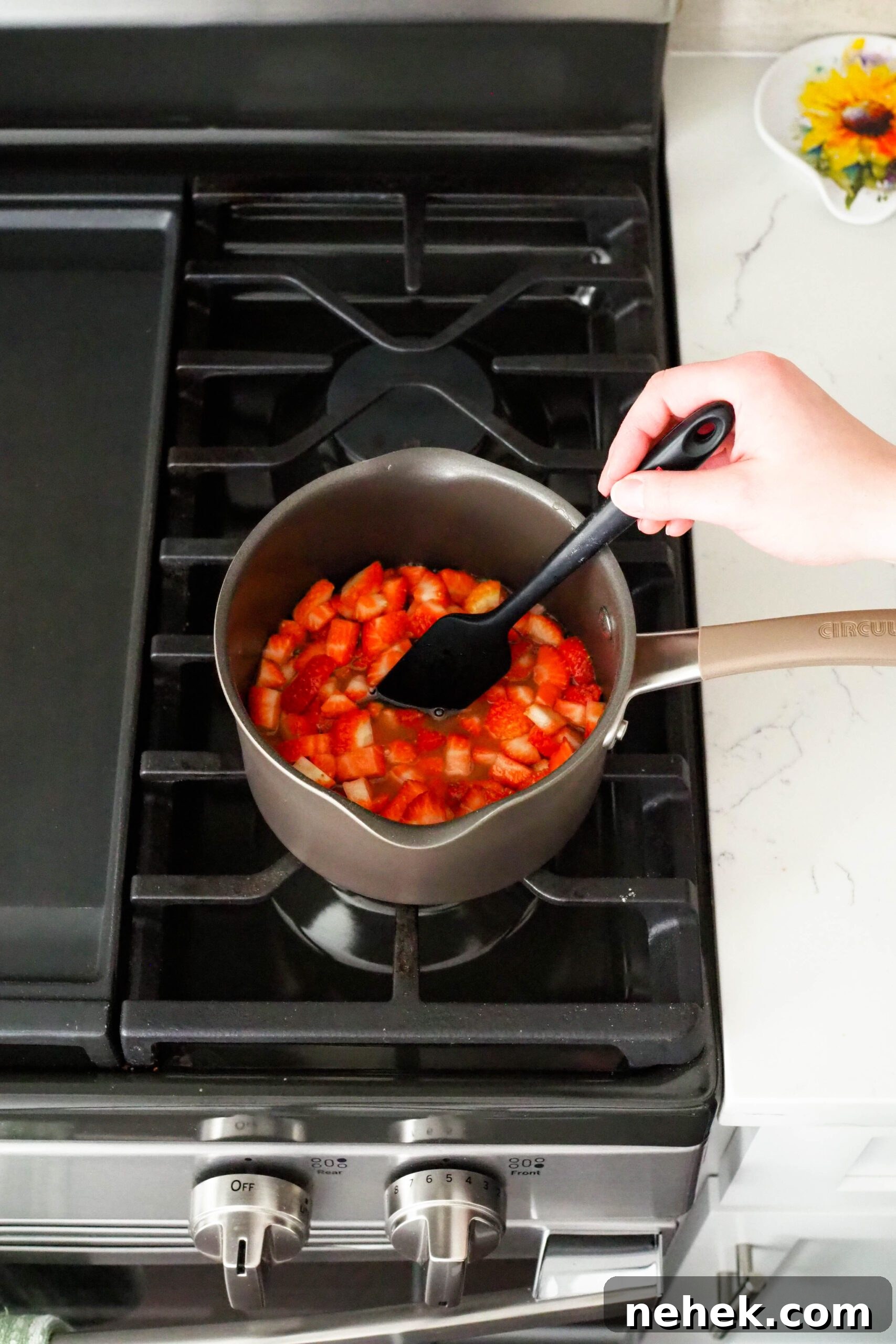 A black spatula stirs a pot of diced strawberries.