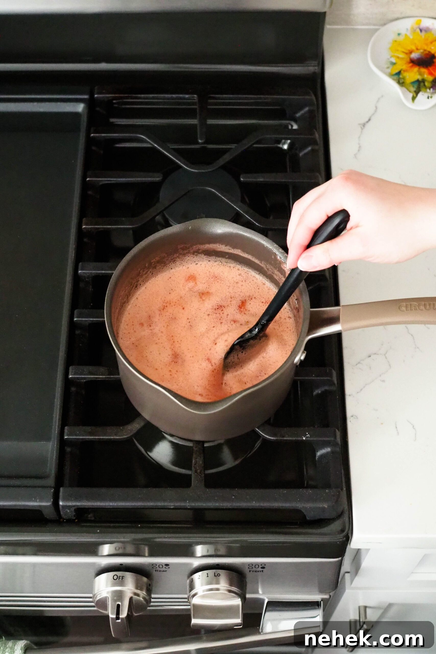 A black spatula stirs a pot of bubbling diced strawberries.
