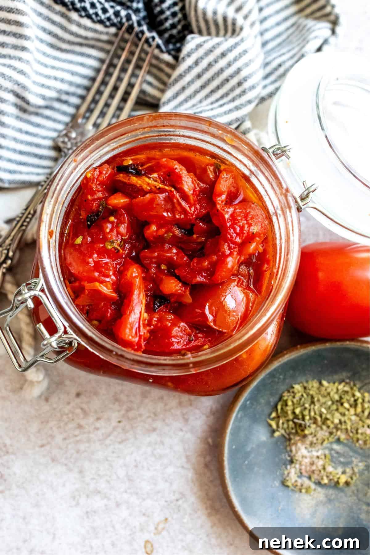 Large jar with fire roasted tomatoes in it. A fork and dried herbs to the side.