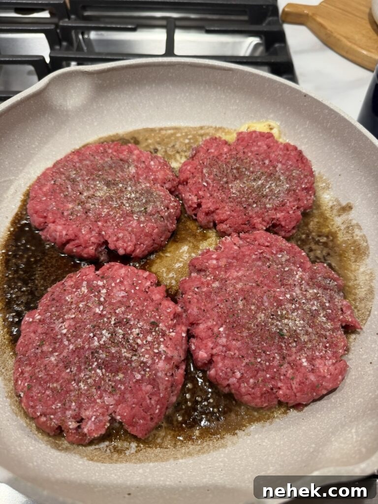 Seasoned burger patties sizzling in the pan