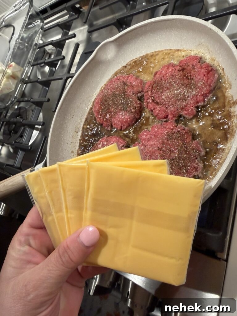 Slices of American cheese held over the sizzling burgers