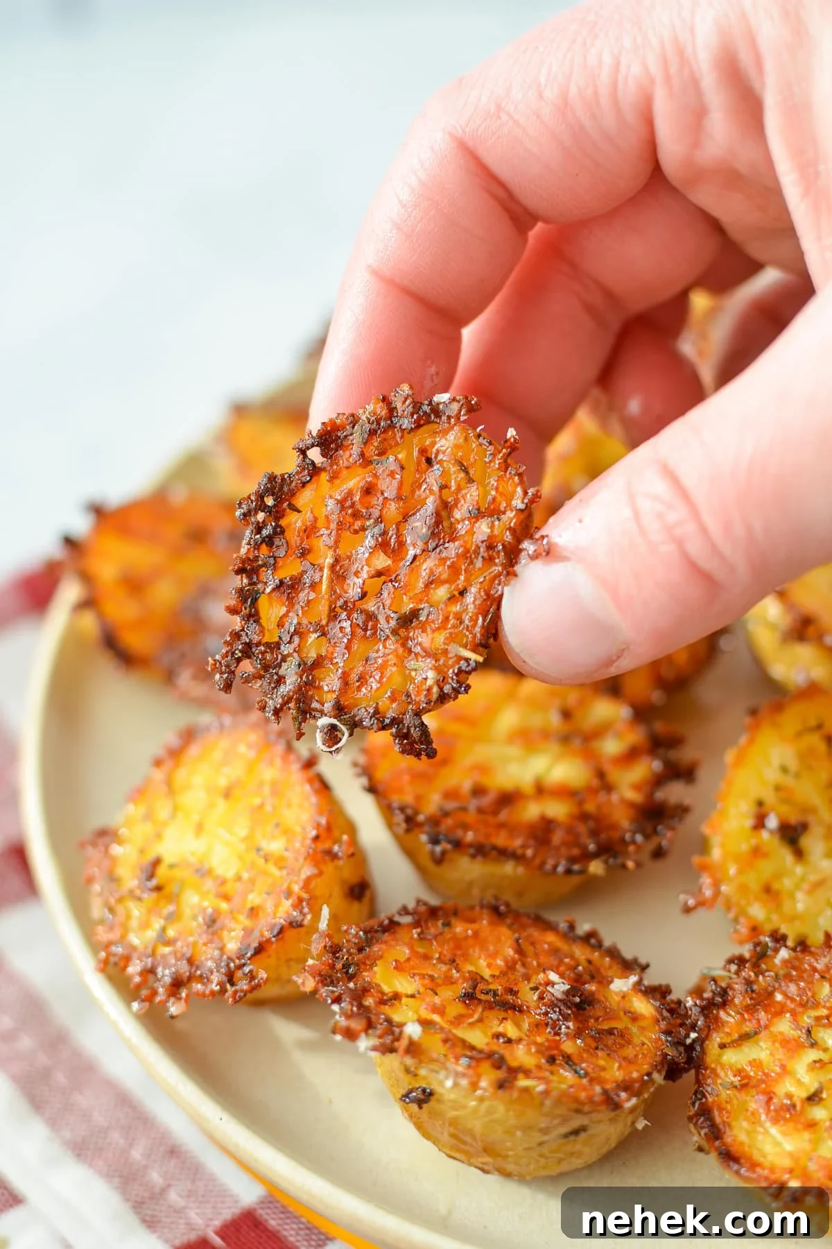A hand taking a small potato from a plate of roasted parmesan potatoes.
